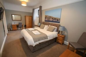 A bedroom with a bed, bedside table, chair, desk, and a painting on the wall. - The Royal Hotel Stromness (Stromness)
