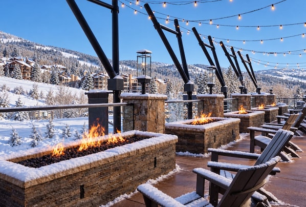 Outdoor seating with fire pits, snow-covered landscape, and string lights.