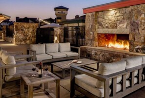 An outdoor seating area with a stone fireplace, sofas, and a table with wine glasses. - Cozy Christmas Ski Getaway \ Sheraton Steamboat Studio \ Dec 25–30 (Steamboat Springs)