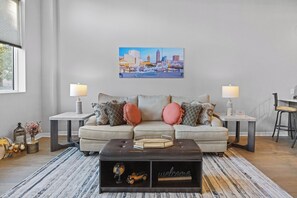 A living room with a sofa, two side tables, a coffee table, and a cityscape painting on the wall. - 15-ft Ceilings · Cozy Tremont Loft · Free Parking (Cleveland)