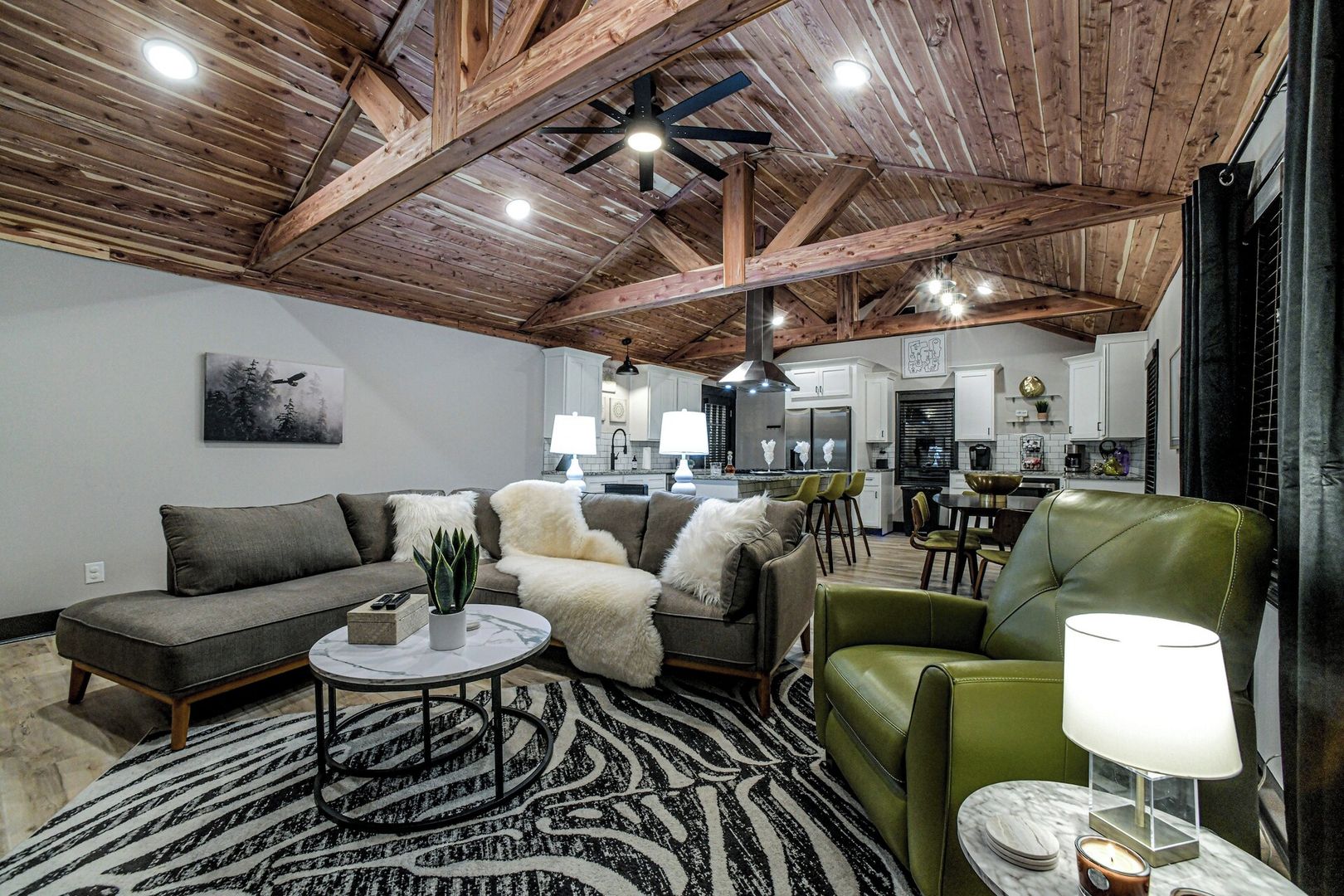 A modern living room with a wooden ceiling, a sofa set, a green armchair, and a patterned rug.