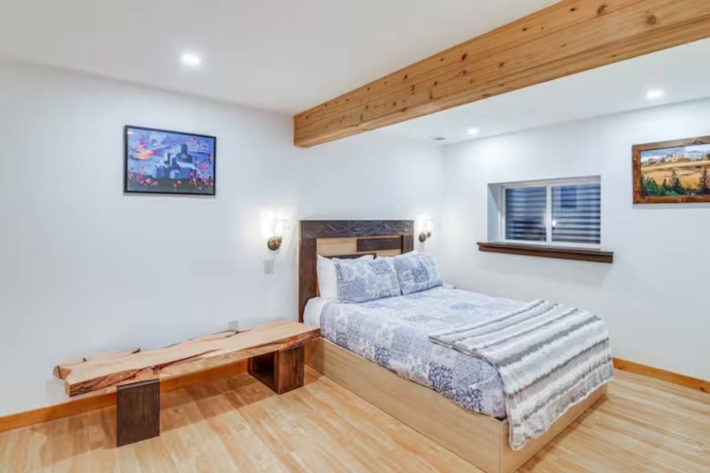 Une chambre à coucher comprenant un lit, un banc, une fenêtre et deux lampes fixées au mur.