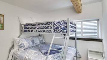 A bunk bed with a ladder, a bedside table, and a window with blinds.