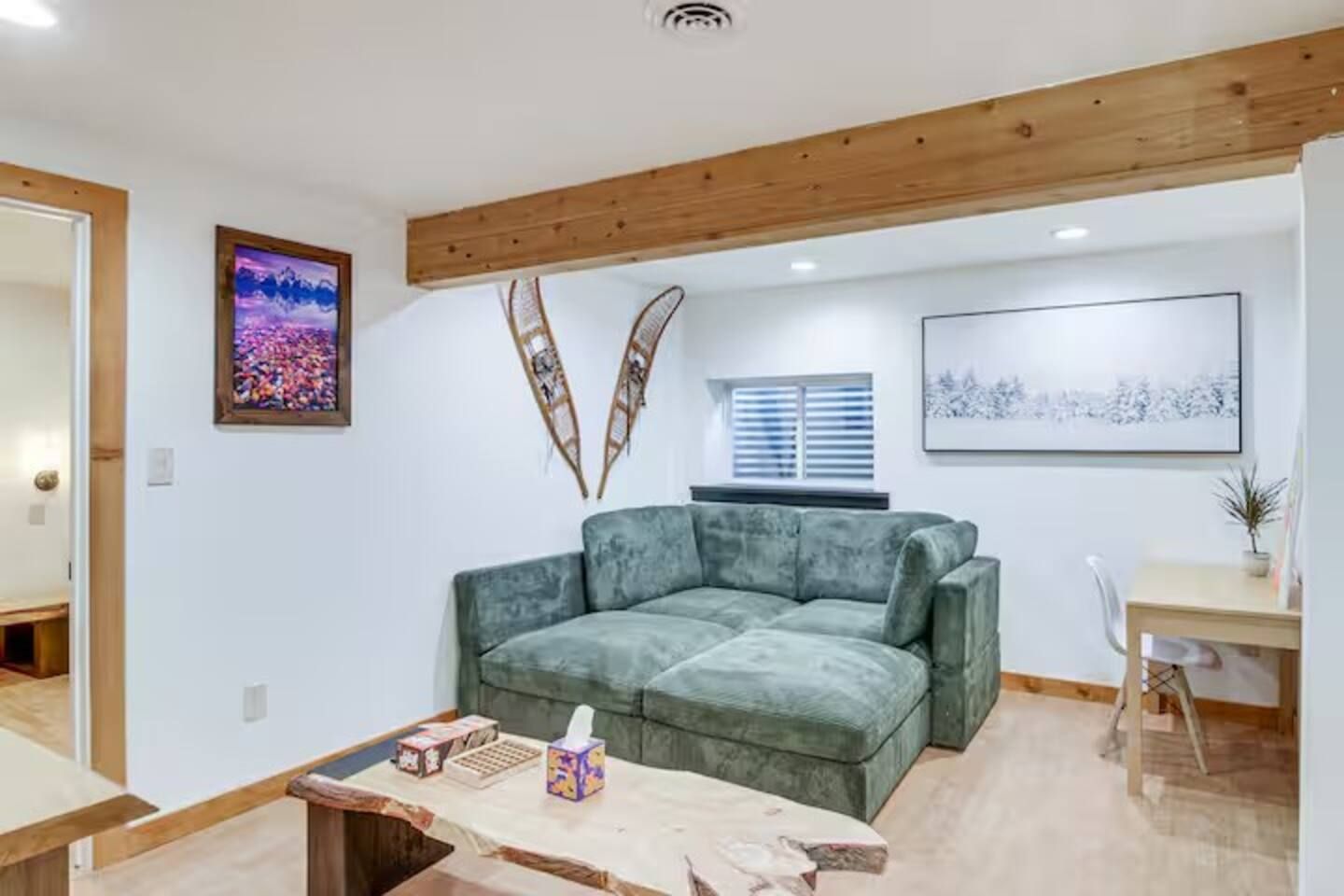 A living room with a green sofa, wooden ceiling beams, a window with blinds, and a framed picture on the wall.