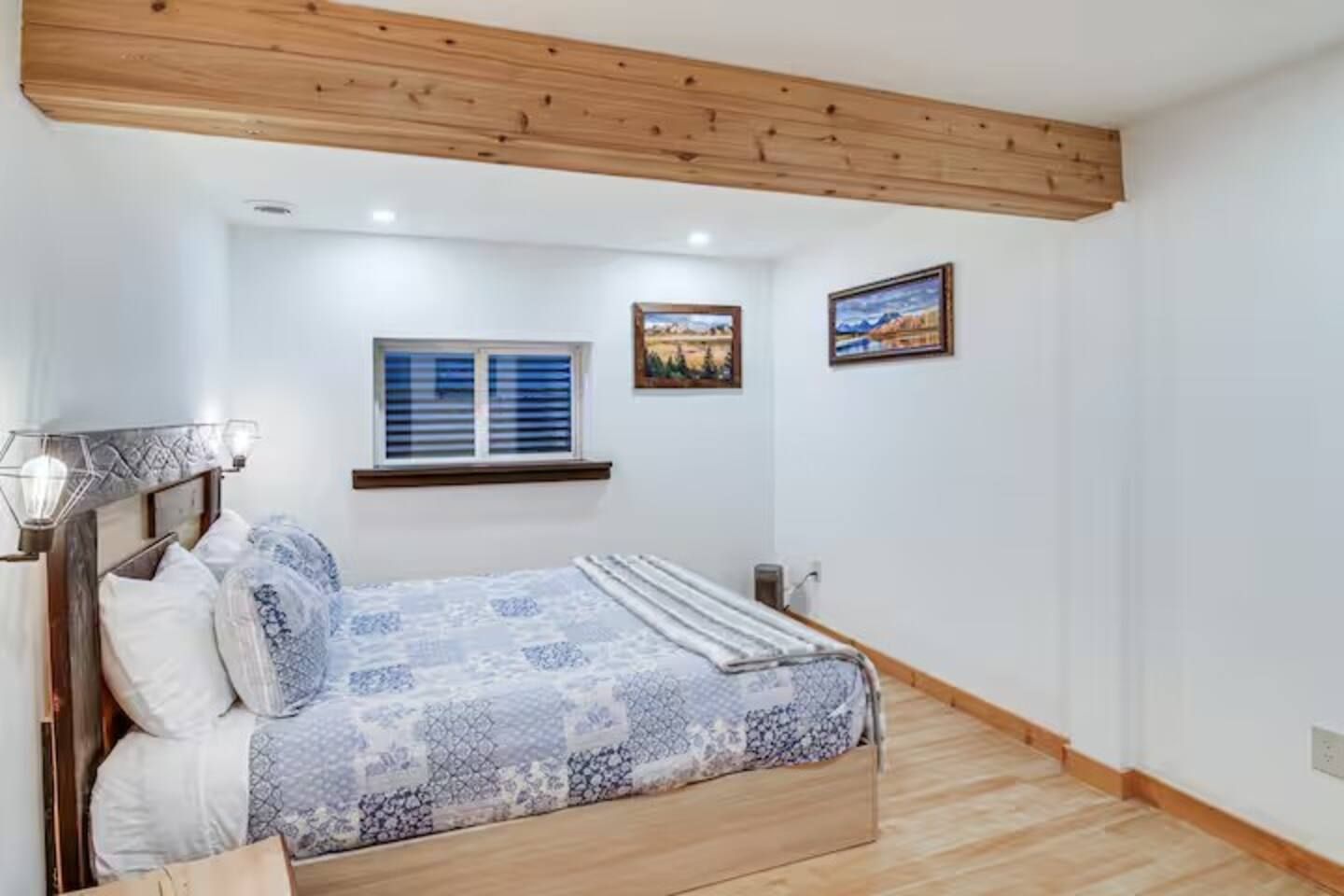 A bedroom with a bed, a window with blinds, a wall-mounted picture, and a wooden ceiling.