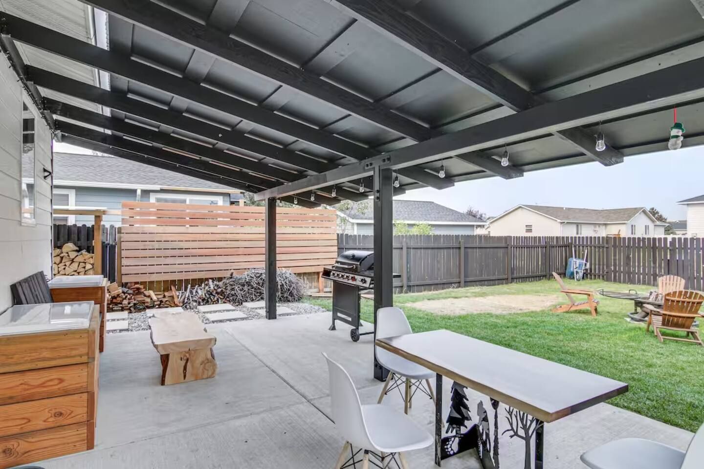 A covered patio area with a barbecue grill, outdoor seating, and a wooden fence in the background.