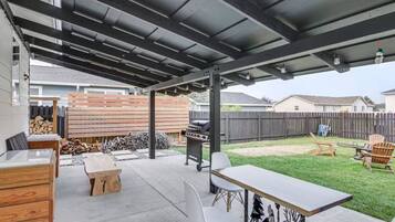 A covered patio area with a barbecue grill, outdoor seating, and a wooden fence in the background.