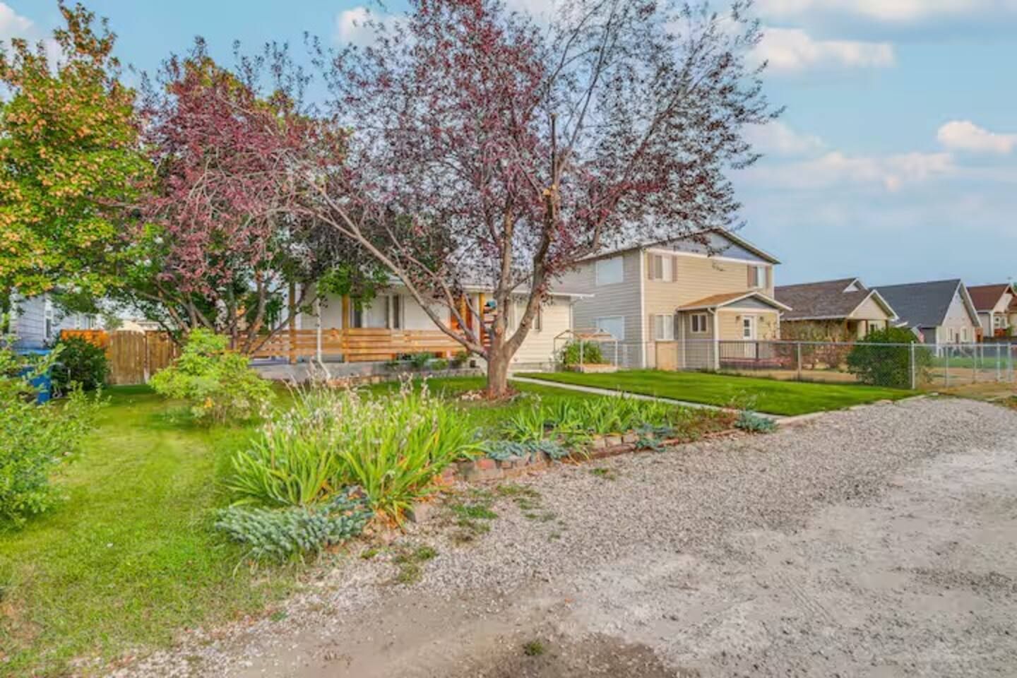 A residential area with a two-story house, a well-maintained lawn, and a gravel driveway.