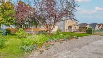 A residential area with a two-story house, a well-maintained lawn, and a gravel driveway.