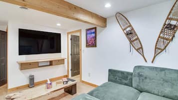 A living room with a TV, wooden beams, a green sofa, and a wall-mounted shelf.