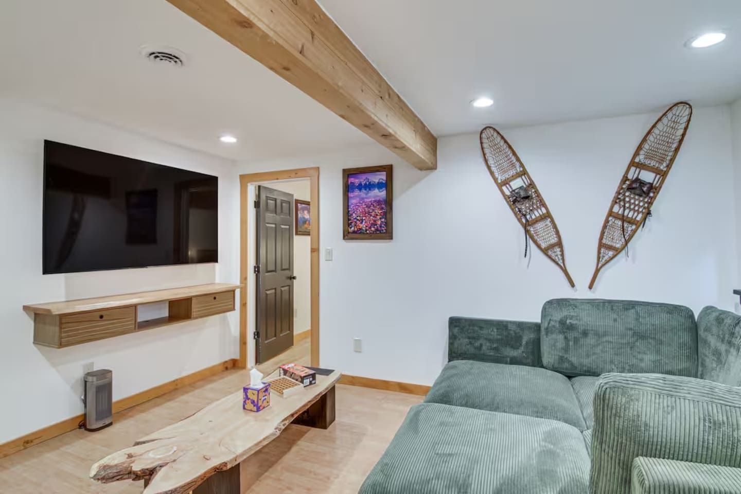 Un salon équipé d’un téléviseur à écran plat, d’un banc en bois, d’un canapé vert et de deux éléments décoratifs fixés au mur.