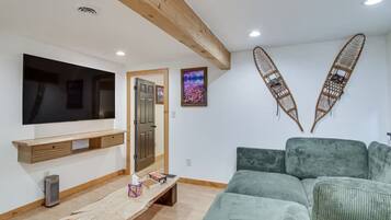 Un salon équipé d’un téléviseur à écran plat, d’un banc en bois, d’un canapé vert et de deux éléments décoratifs fixés au mur.