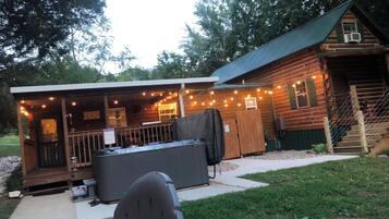 A wooden cabin with a porch, outdoor seating, and a hot tub.