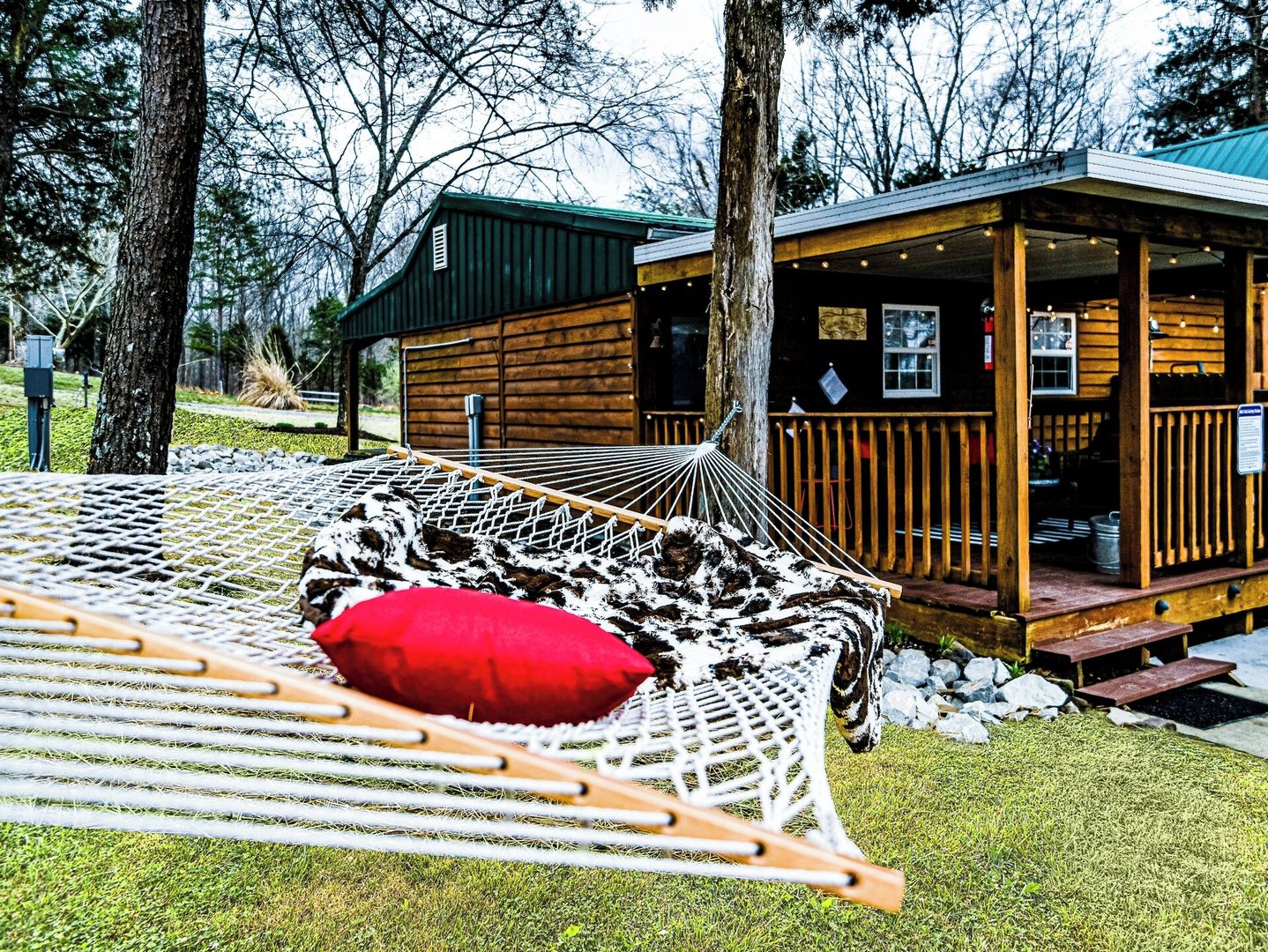 A hammock with a red pillow, a wooden deck, and a cabin with a porch.