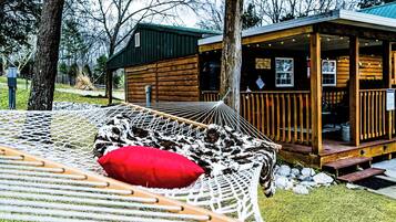 A hammock with a red pillow, a wooden deck, and a cabin with a porch.
