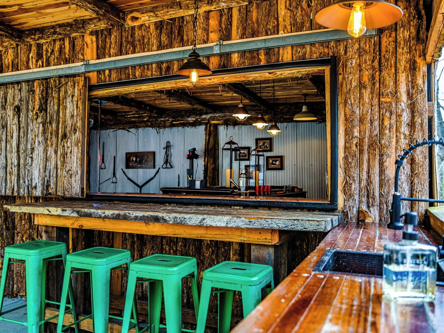 Un coin bar au style rustique, avec des murs en bois, un grand miroir et des tabourets verts.