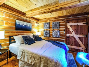 A wooden cabin interior with a bed, wall-mounted artwork, and a rustic door.