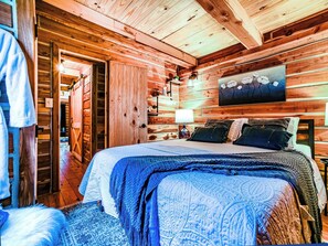 A wooden cabin interior with a bed, a painting, and a wooden door.