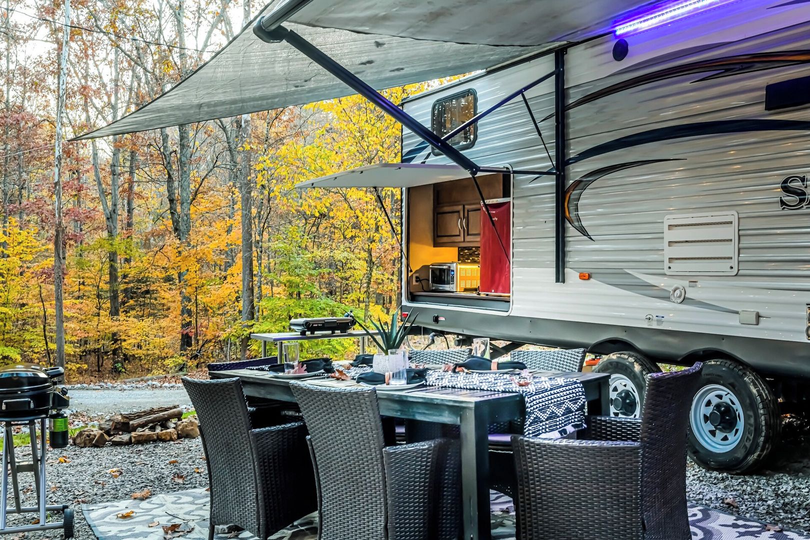 Uma motorhome com cozinha, mesa e cadeiras montadas ao ar livre.