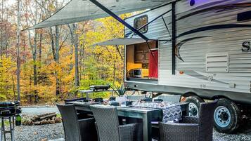 Uma motorhome com cozinha, mesa e cadeiras montadas ao ar livre.