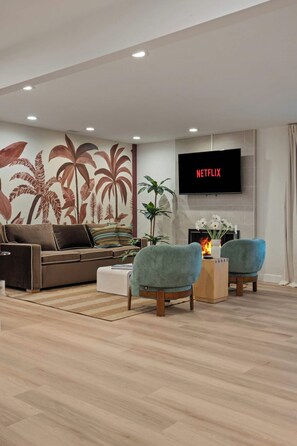 Ein modernes Wohnzimmer mit einer Couch, zwei Sesseln, einem Couchtisch, einem Kamin und einem an der Wand befestigten Fernseher.