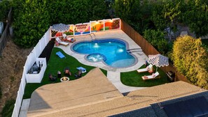 Un patio trasero con piscina, sillas de descanso, bañera de hidromasaje y zona de barbacoa.