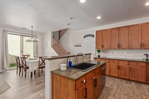 A modern kitchen with wooden cabinets, a built-in sink, and a dining area with a table and chairs. - 3-bedroom house in adorable Mesa with cool AC breeze (Mesa)