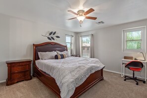 A bedroom with a bed, a desk, a chair, a nightstand, a ceiling fan, and a window. - 3-bedroom house in adorable Mesa with cool AC breeze (Mesa)