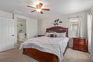 A bedroom with a wooden bed, a ceiling fan, a window with blinds, and a door leading to a bathroom. - 3-bedroom house in adorable Mesa with cool AC breeze (Mesa)