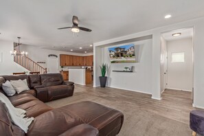 A spacious living room with a brown leather sectional sofa, a ceiling fan, and a kitchen in the background. - 3-bedroom house in adorable Mesa with cool AC breeze (Mesa)
