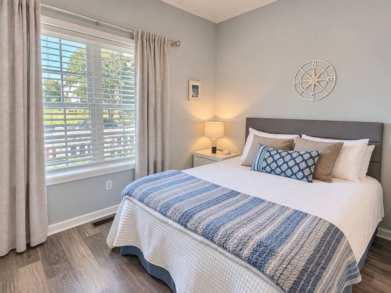 Un dormitorio con cama, mesita de noche, lámpara y ventana con cortinas.