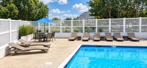 Ein Poolbereich mit Liegestühlen und einem Tisch, umgeben von einem weißen Zaun.