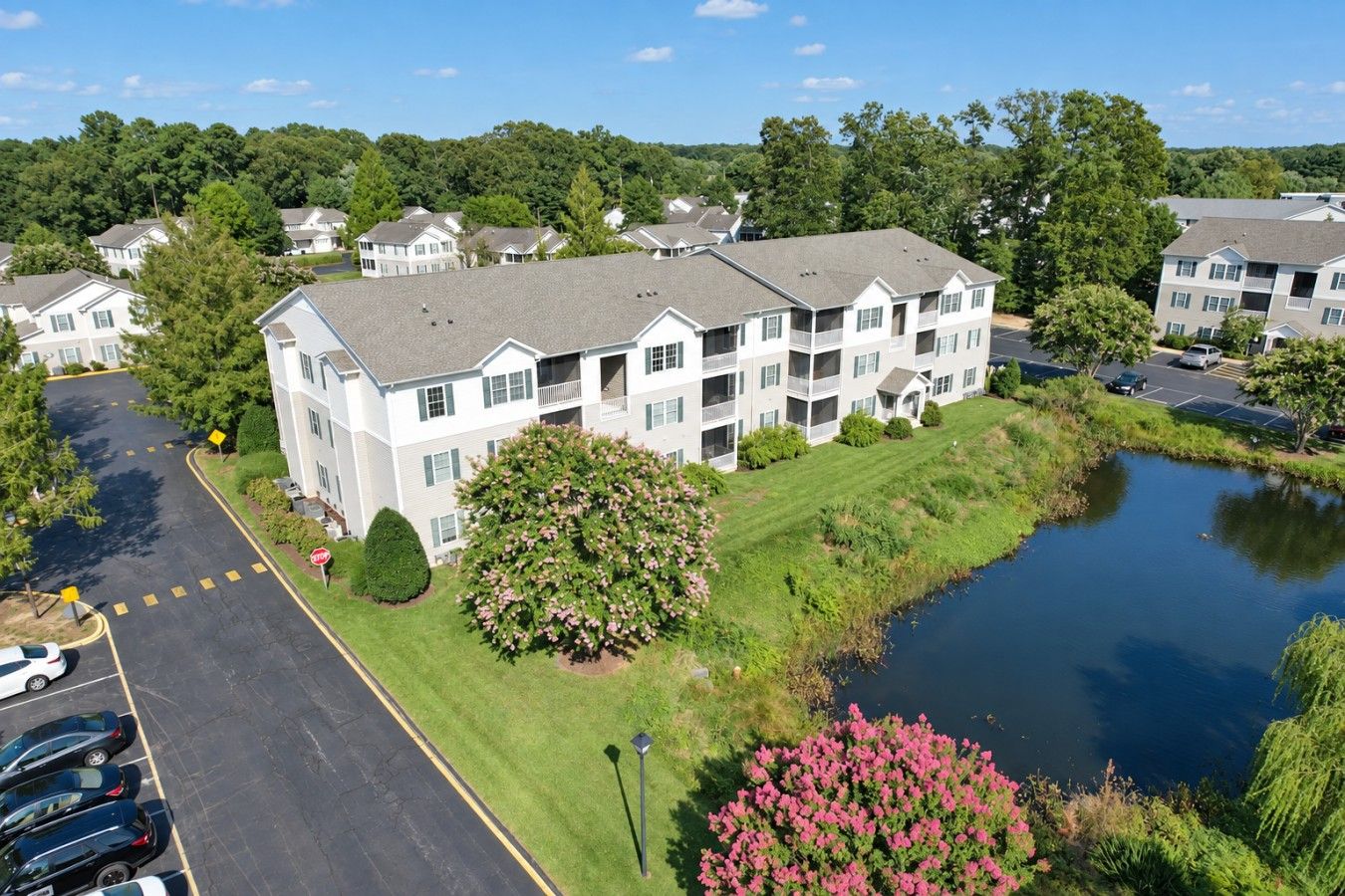 A multi-story residential building with a parking lot and a small body of water.