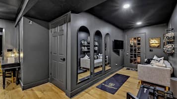A modern interior with a grey wall, a wooden floor, a grey sofa, a black exercise machine, and a door leading to another room.