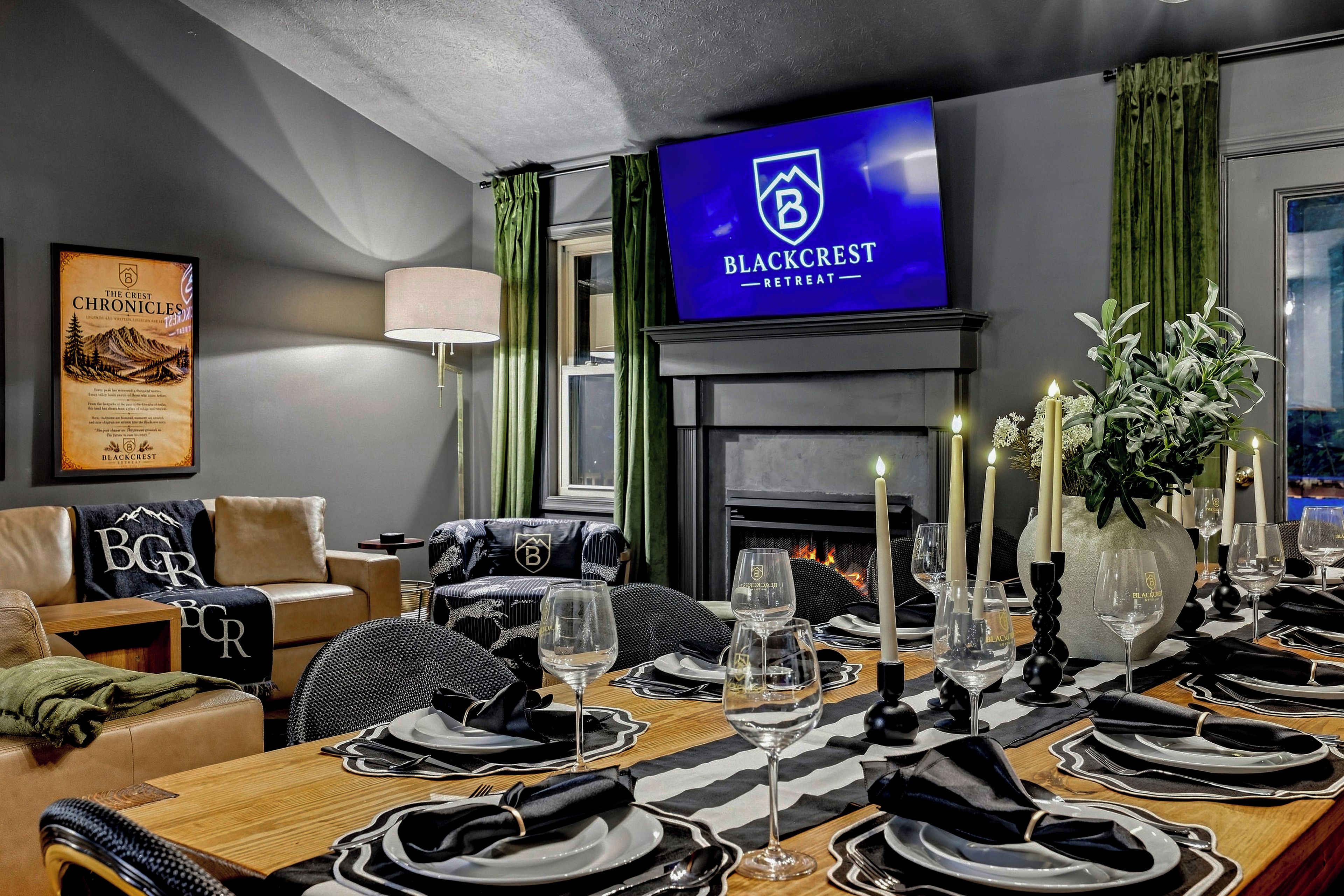 A well-appointed dining area with a fireplace, a television displaying 'BLACKCREST RETREAT', and a cozy seating arrangement.