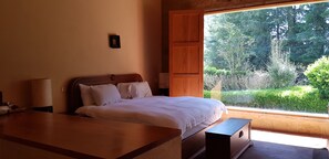 Ein Schlafzimmer mit einem Bett, Nachttischen und Blick auf Grünfläche.