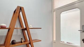 Ein Holzladderschrank mit dekorativen Gegenständen vor einer hellen Wand, eine weiße Tür mit satiniertem Glasfenster und eine schwarze Fußmatte.