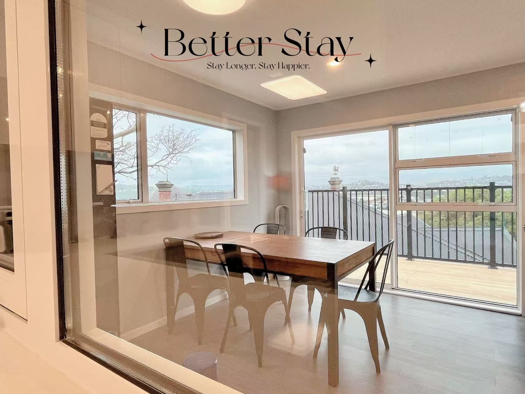 A room with a dining table and chairs, large windows, and a balcony with a view.