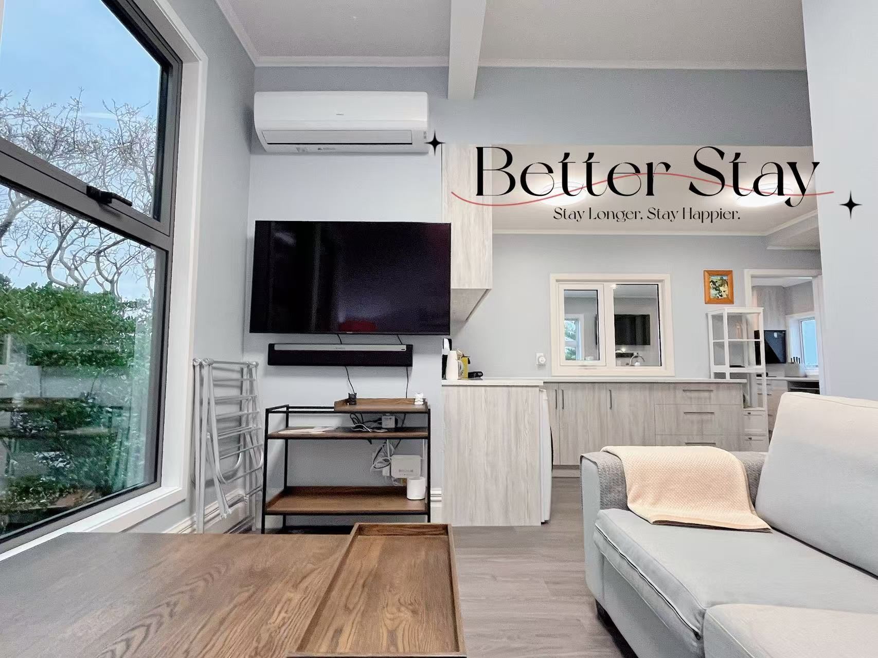 A modern living room with a large window, a flat-screen TV, a wooden coffee table, and a light-colored sofa.