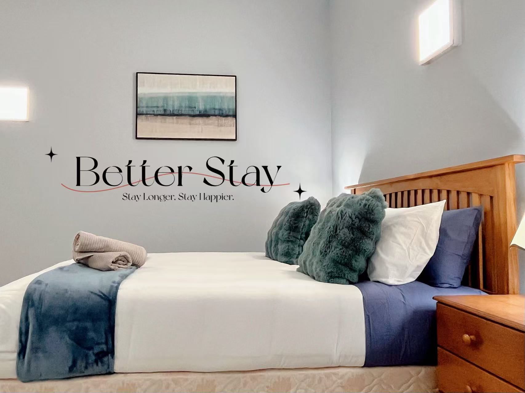 Ein Schlafzimmer mit einem Bett, Kissen, einem Nachttisch und einer Wand mit einem motivierenden Zitat.