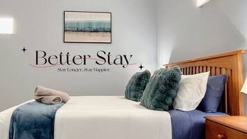 Ein Schlafzimmer mit einem Bett, Kissen, einem Nachttisch und einer Wand mit einem motivierenden Zitat.