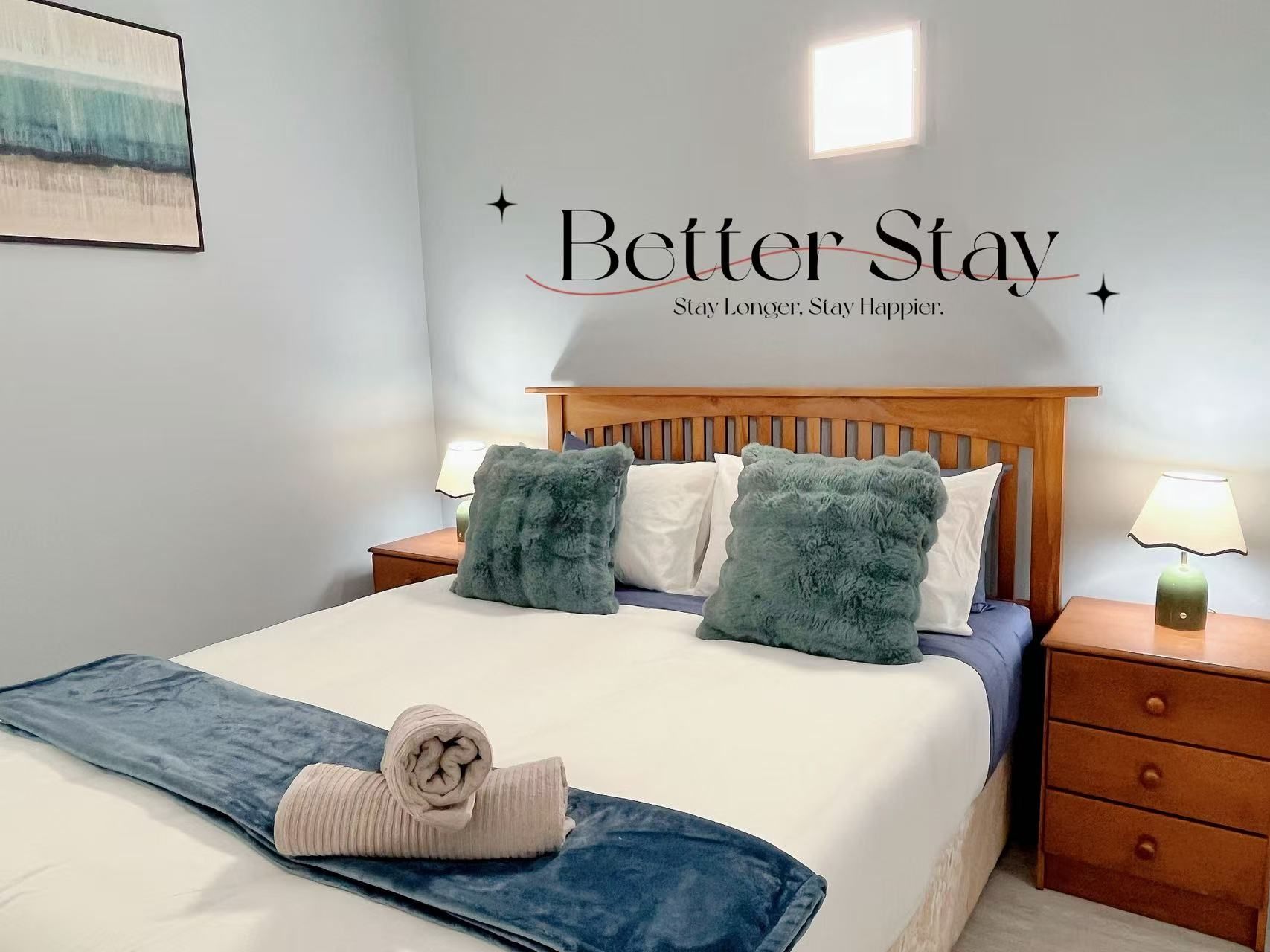 A hotel room with a bed, two bedside tables, a headboard, and a wall with a motivational message.