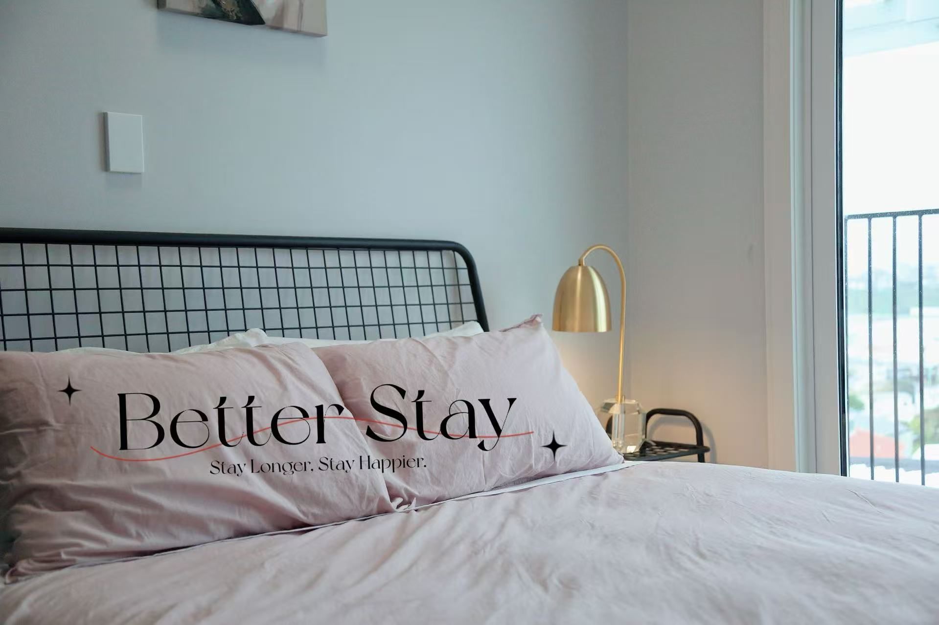 Ein ordentlich bezogenes Bett mit einem Kissen, das den Text 'Better Stay' und einen motivierenden Spruch zeigt.
