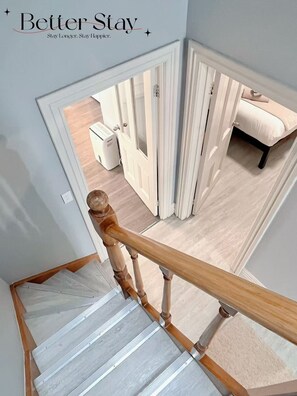 A staircase with a wooden handrail leading to a room with a bed and a white radiator.