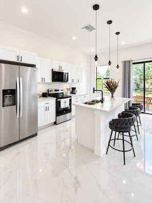 A modern kitchen with white cabinets, stainless steel appliances, and a marble floor. - The Gray House, Modern Comfort (Lehigh Acres)