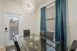 A dining area with a glass table and chairs, a ceiling light fixture, and a door with a window. - South-Facing Pool • Lazy River • Arcade Game Room • Gated Resort • Near Disney (Four Corners)