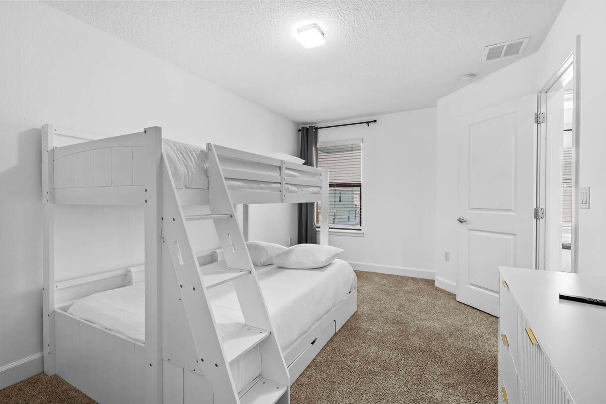 Une chambre avec des lits superposés, une porte blanche et une fenêtre avec des stores.