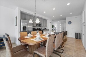 Een moderne keuken met een eethoek, voorzien van roestvrijstalen apparatuur, een houten eettafel en barstoelen.