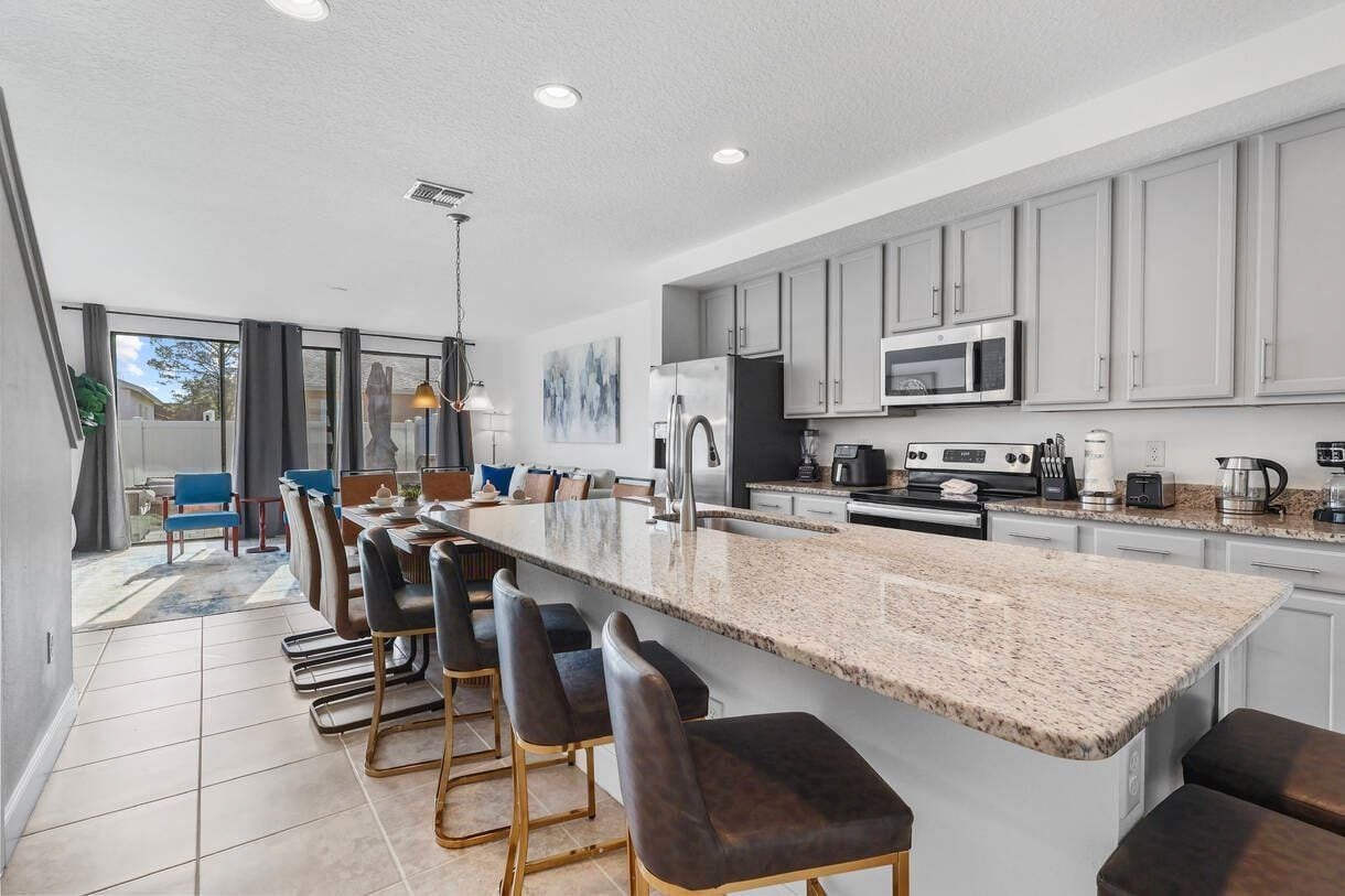 Una cocina moderna con una isla grande, taburetes de bar y un comedor con sillas azules.