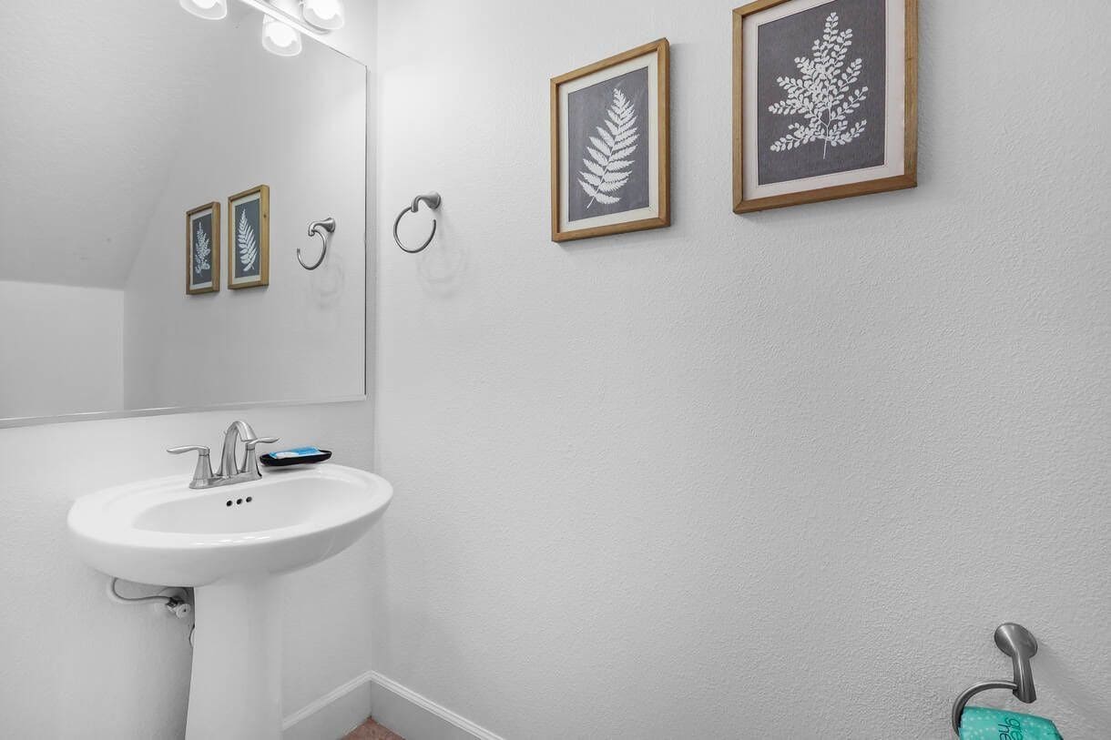 Un baño con un lavamanos blanco, un espejo e impresiones botánicas enmarcadas en la pared.